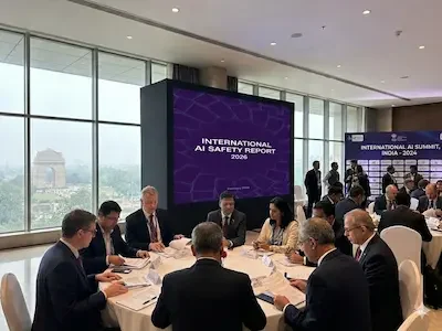 Mehrere Personen sitzen an einem Konferenztisch vor einer Leinwand mit dem Titel „International AI Safety Report 2026“.